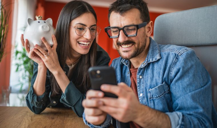 couple take a self portrait or video call on mobile phone while hold piggy bank at home